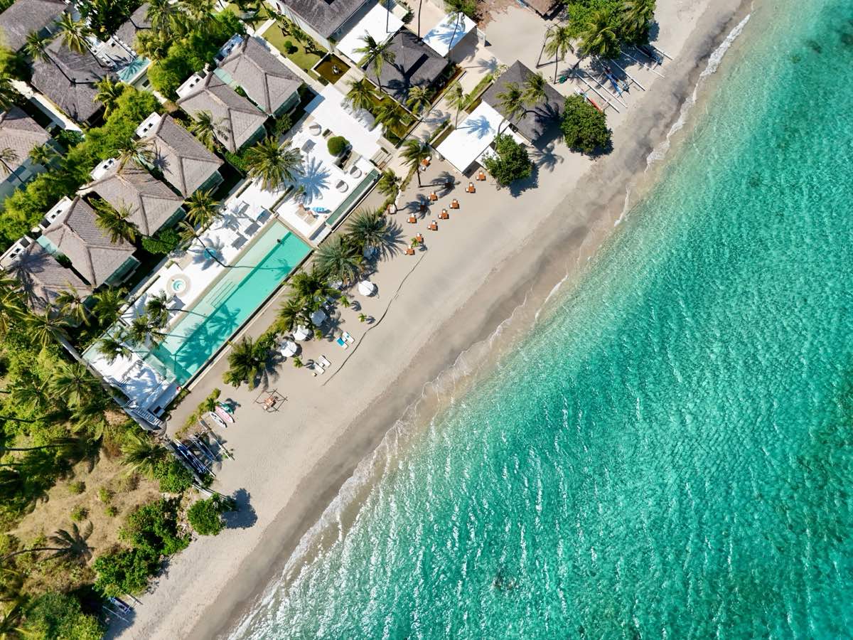 ภาพมุมสูงของรีสอร์ตวิลล่าริมหาดบน Koh Samui มีสระว่ายน้ำยาว วิลล่าใต้ร่มเงามะพร้าว หาดทรายขาว และทะเลสีเทอร์ควอยซ์ใส