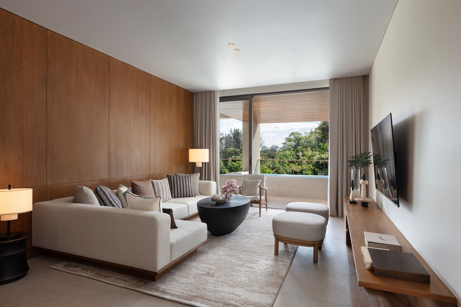 Living room of the three-bedroom show condominium at Kiara Reserve Residences, Layan Bay: teak wall, cream sofa and the terrace with its jacuzzi pool beyond