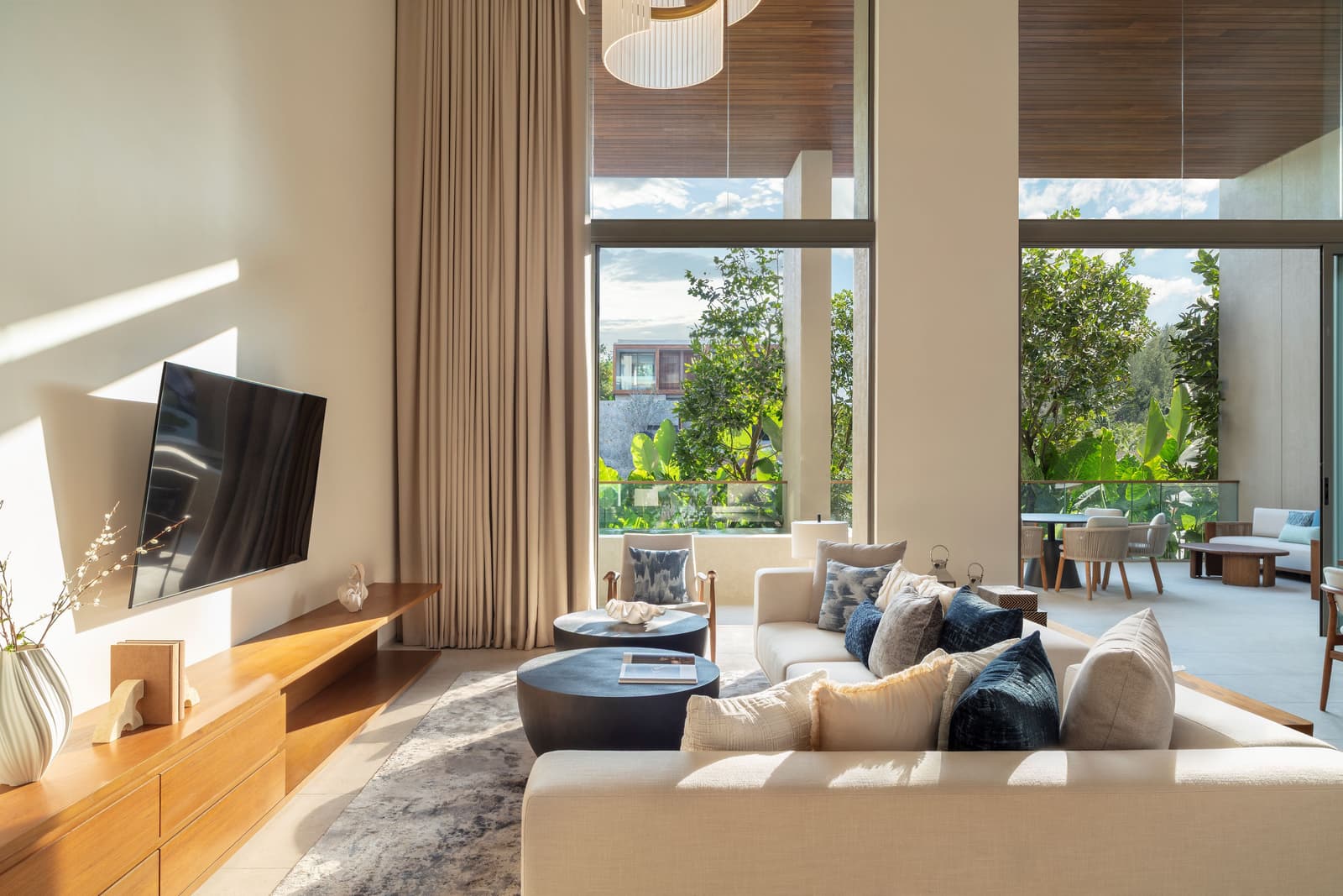 Living room of the three-bedroom duplex show condominium at Kiara Reserve Residences, Phuket, with a teak media wall and the terrace beyond