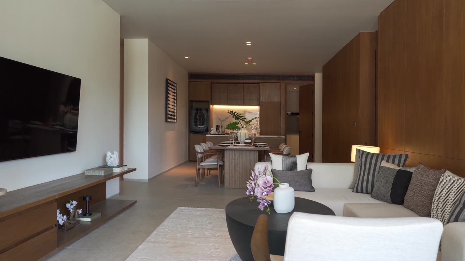 Гостиная и открытая кухня шоу-кондоминиума с тремя спальнями в Kiara Reserve Residences, Пхукет, в светлом камне и орехе
