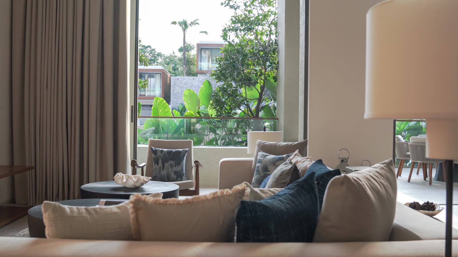 The living room of the three-bedroom duplex show home at Kiara Reserve Residences, Phuket, sofas facing tall windows onto a garden terrace