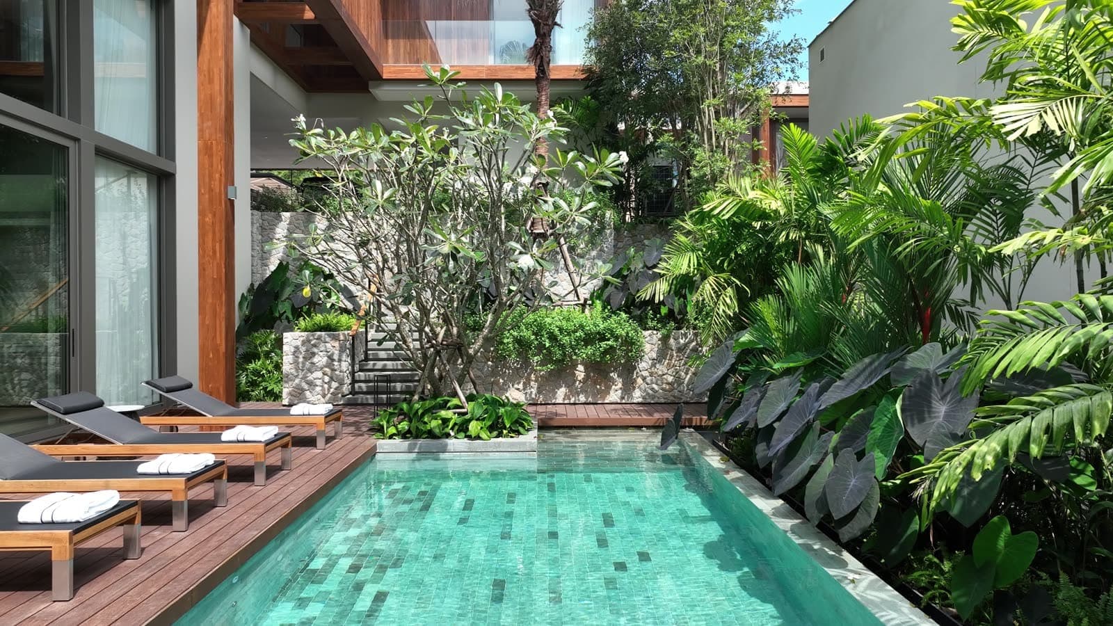 The private pool of the four-bedroom show villa at Kiara Reserve Residences, Layan Bay, Phuket: turquoise tiles, a timber deck with loungers, a jungle garden around it