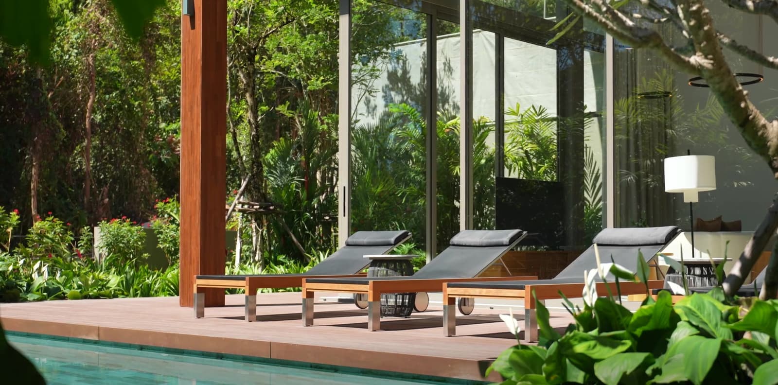 Pool terrace of a show villa at Kiara Reserve Residences above Layan Bay, Phuket: sun loungers on a timber deck beside the pool, jungle behind