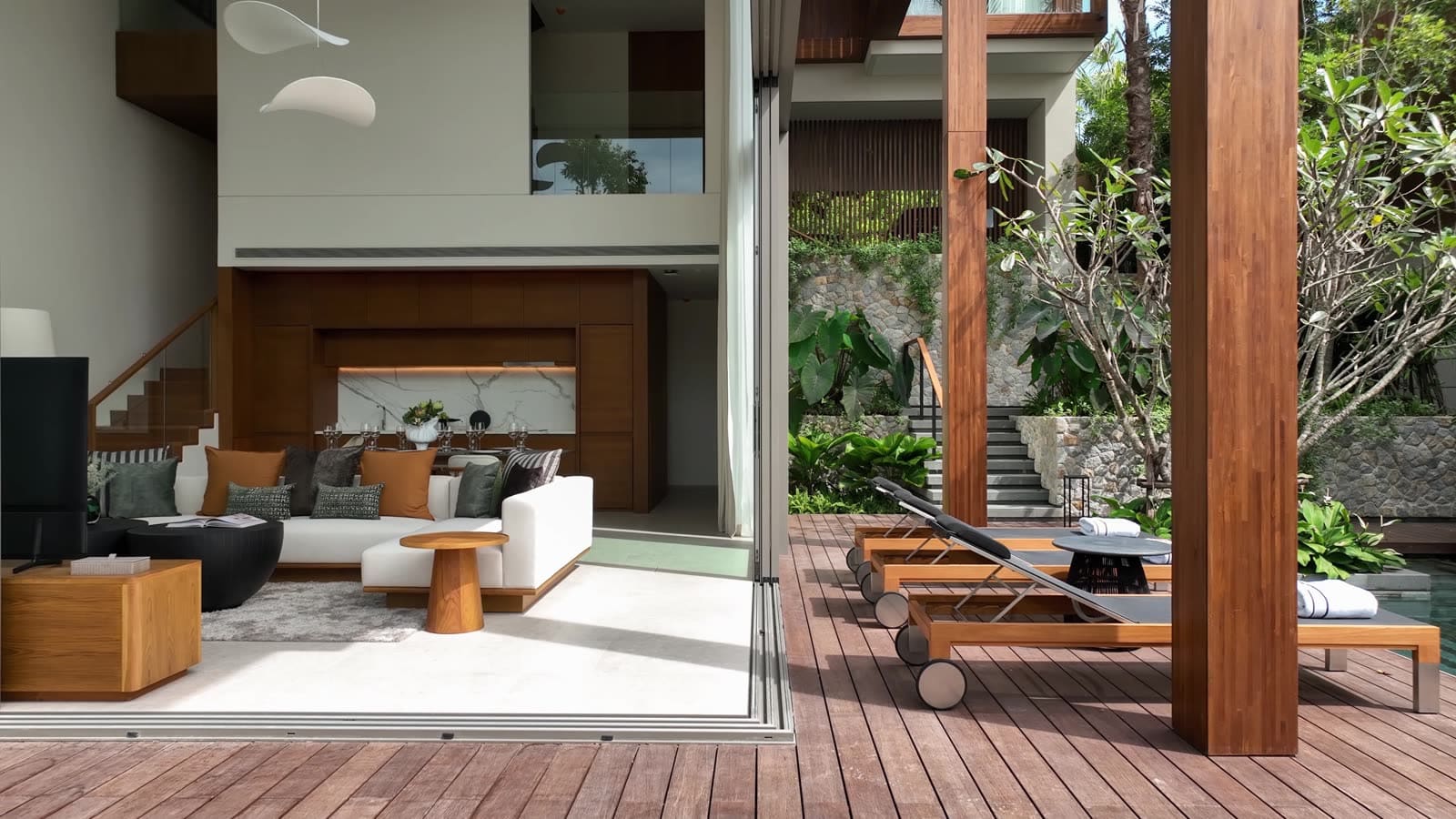 วิลลาตัวอย่าง 3 ห้องนอนที่ Kiara Reserve Residences ภูเก็ต ห้องนั่งเล่นเปิดออกสู่เด็คไม้ริมสระพร้อมเก้าอี้อาบแดดและสวนเขตร้อน