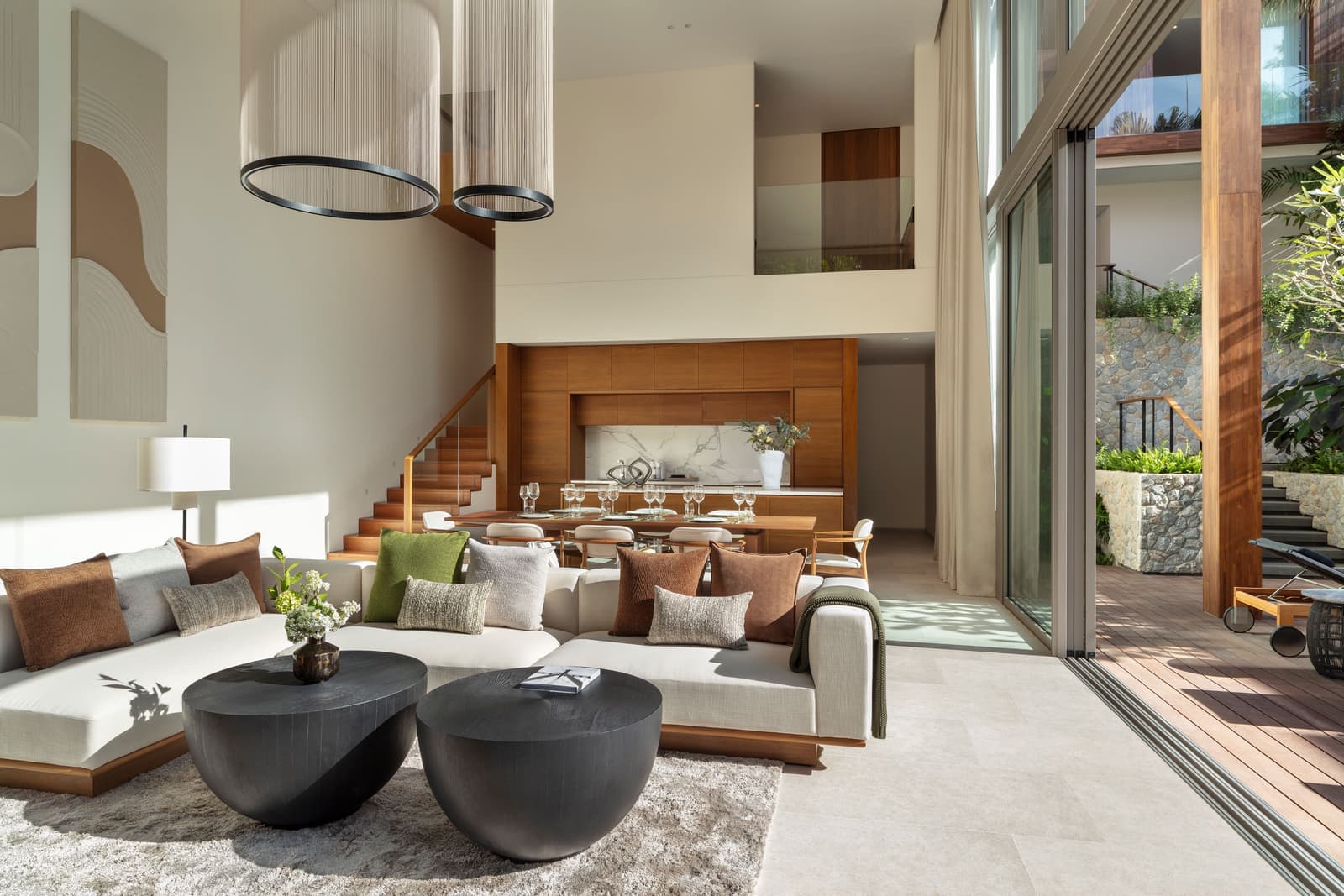 ห้องนั่งเล่นของวิลลาตัวอย่าง 4 ห้องนอนที่ Kiara Reserve Residences ภูเก็ต: โถงเพดานสูงสองชั้น โซฟาสีเทา โต๊ะอาหาร และสระที่เห็นผ่านกระจก