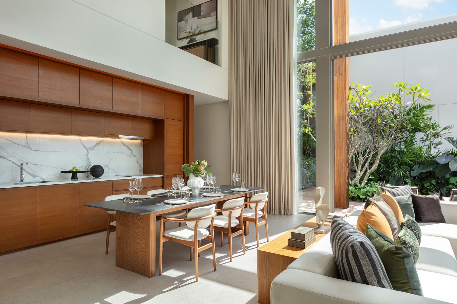 โต๊ะอาหารและครัวเปิดของวิลลาตัวอย่าง 3 ห้องนอนที่ Kiara Reserve Residences ภูเก็ต พร้อมเคาน์เตอร์กลางหินอ่อนและสวนด้านนอก