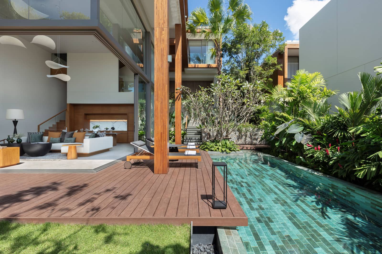 The pool terrace of the three-bedroom show villa at Kiara Reserve Residences, Layan Bay, Phuket: timber deck, private pool, double-height glazed living room and the villas beyond