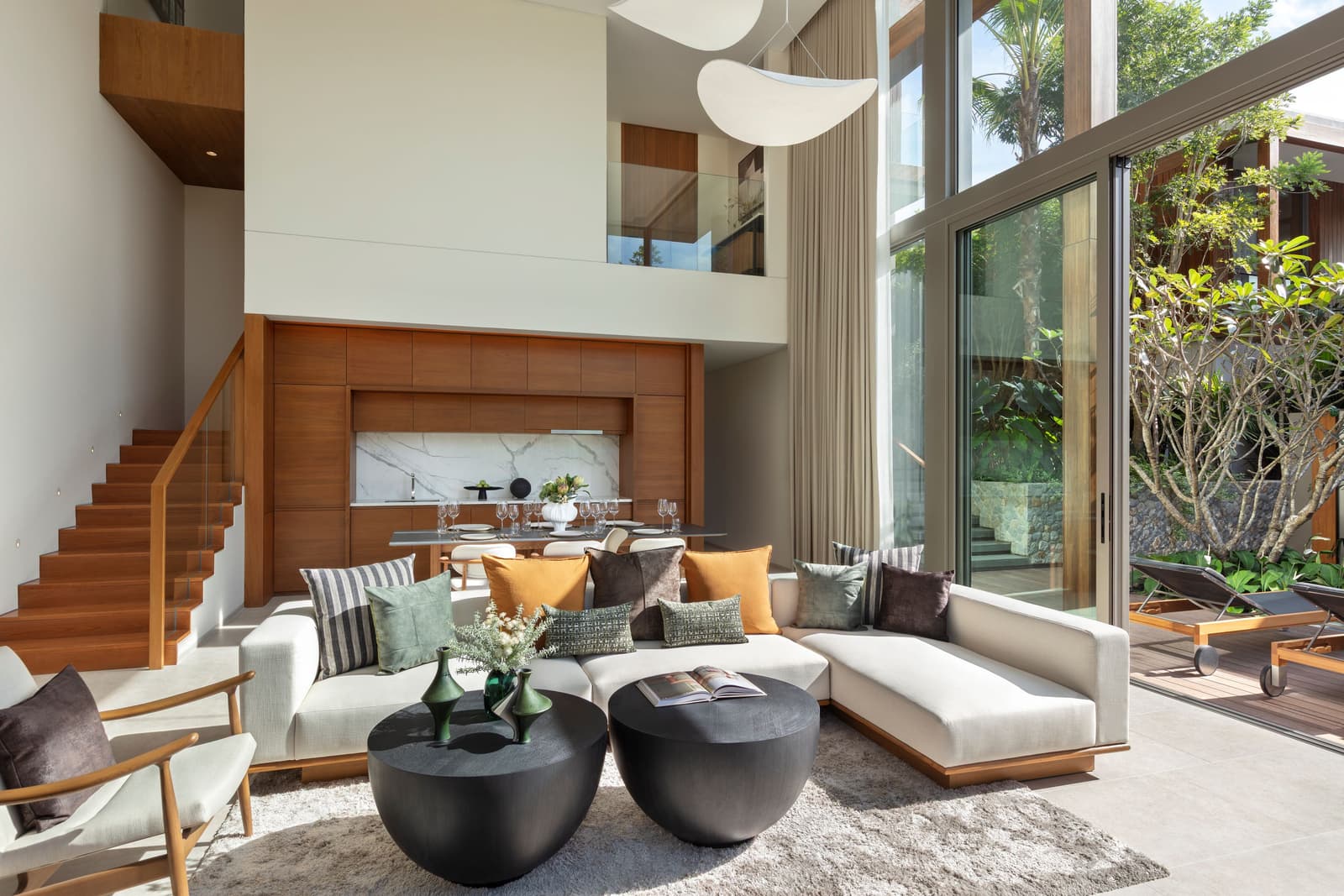 ห้องนั่งเล่นของวิลลาตัวอย่าง 3 ห้องนอนที่ Kiara Reserve Residences อ่าว Layan: เพดานสูงสองชั้น ผนังไม้สัก โซฟาสีขาว และบันไดขึ้นชั้นห้องนอน