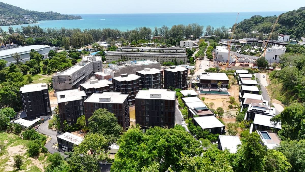 Аэрофотография MGallery Residences MontAzure Lakeside, Kamala, Пхукет, в сентябре 2026 года: готовые тёмные корпуса вокруг озёр, бассейн клубного дома и залив Kamala позади