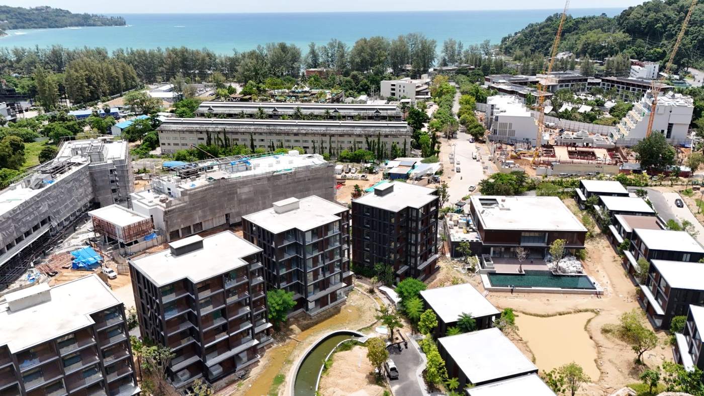 2026 年 9 月 Phuket、Kamala 的 MGallery Residences MontAzure Lakeside 航拍照片:外牆已完成的六層高大樓、會所泳池,以及尚未注水的湖床,遠處是 Kamala 灣