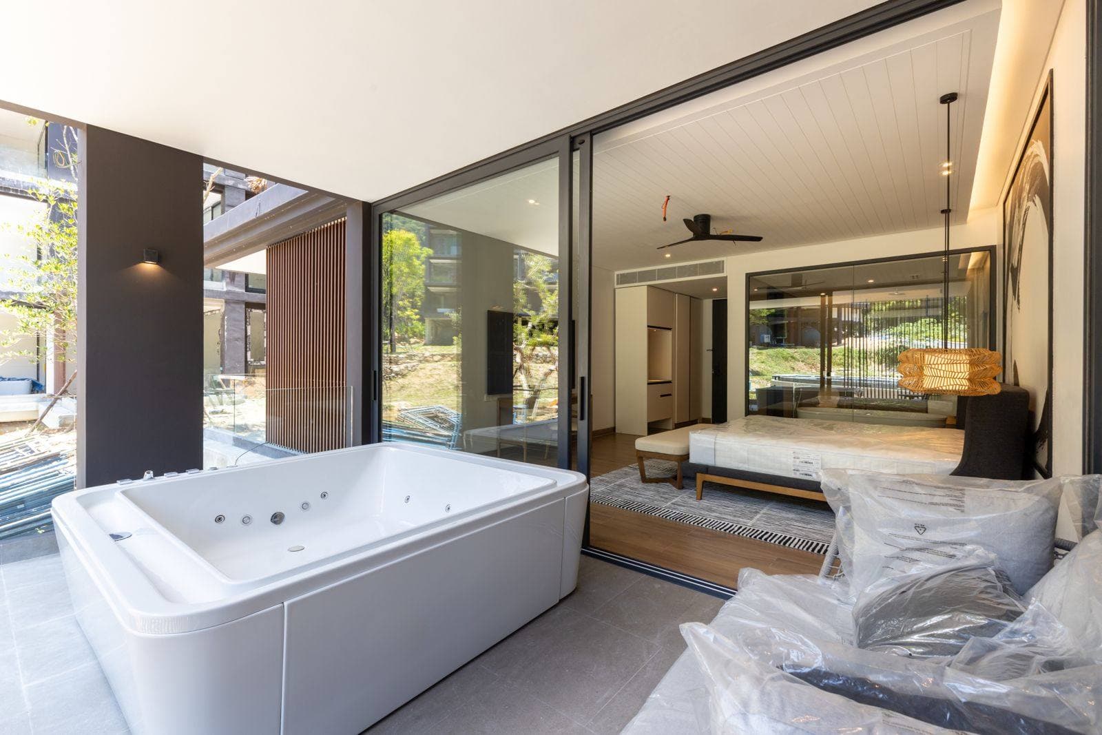 Phuket、Kamala 的 MGallery Residences MontAzure Lakeside 一個地面層住宅的平台:臥室滑動門旁的白色按摩浴缸,戶外沙發仍未拆封