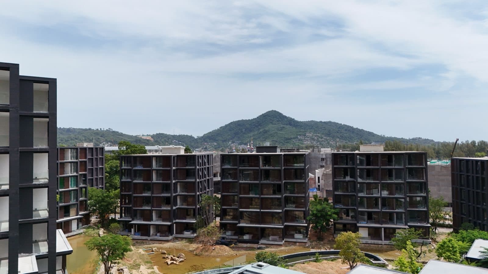 2026 年 9 月 Phuket、Kamala 的 MGallery Residences MontAzure Lakeside 四座已落成的六層高湖畔大樓,望向內陸的山,湖床仍然乾涸