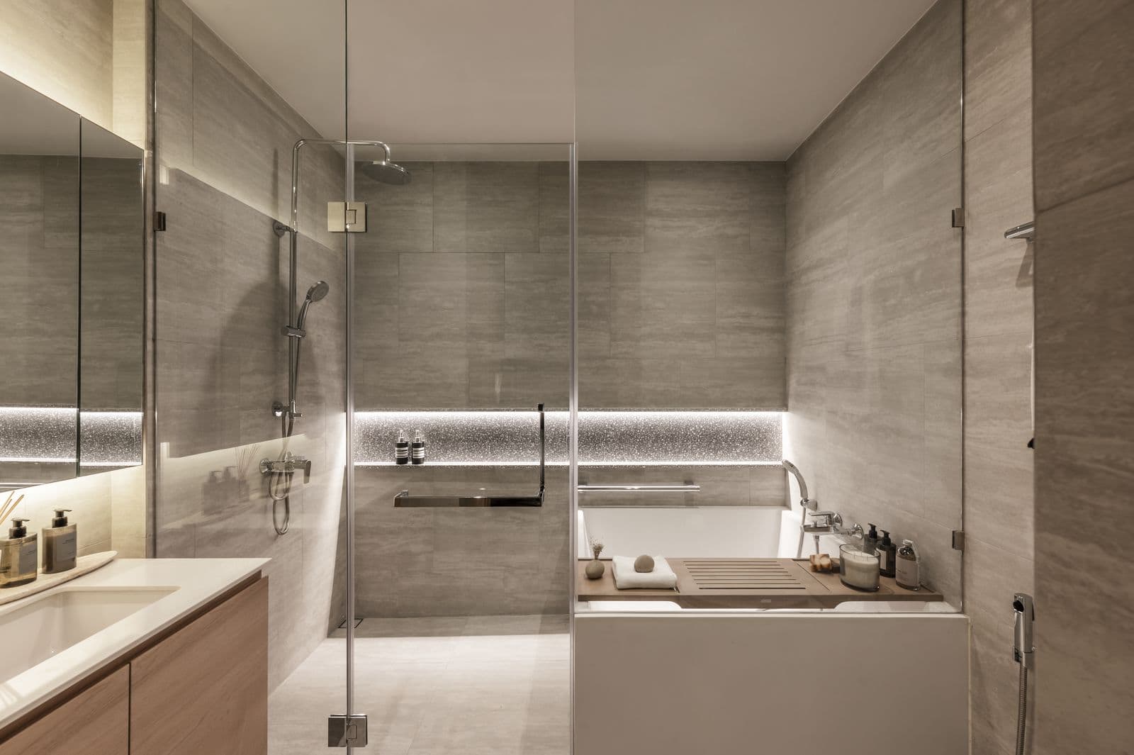 The bathroom of the finished one-bedroom show unit at PEYLAA Phuket: grey stone-look tiles, a glass shower and a square bathtub