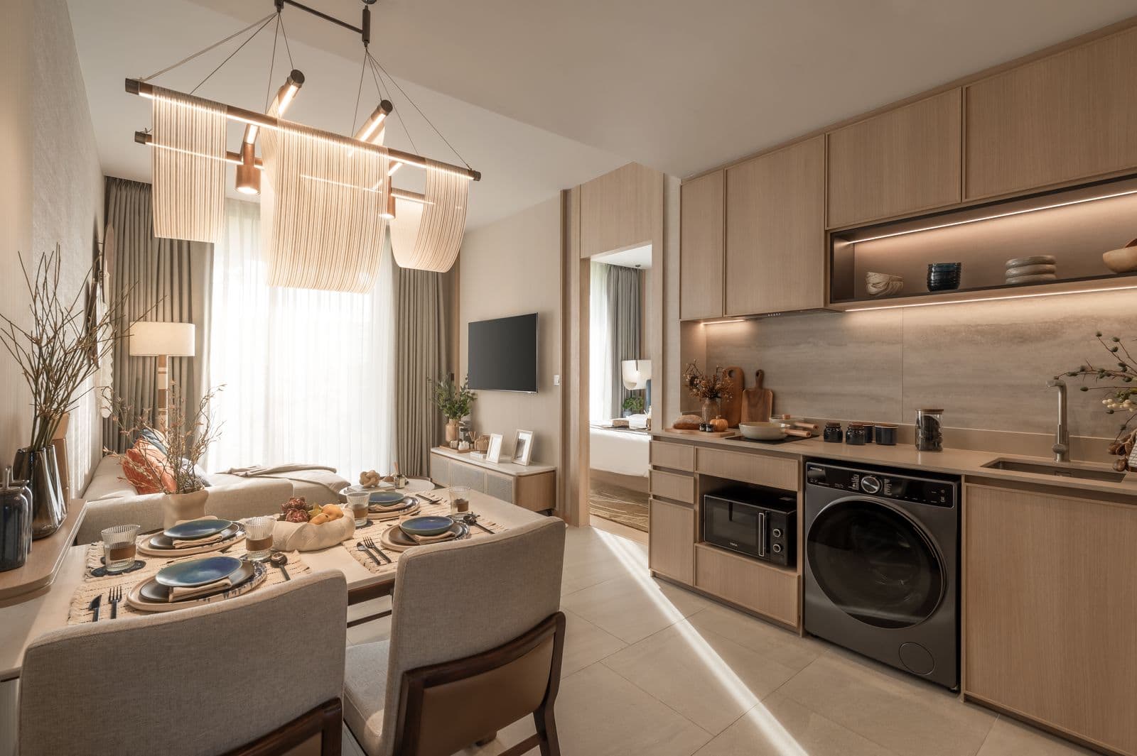 The kitchen of the finished one-bedroom show unit at PEYLAA Phuket: timber cabinets, an induction hob, a washer-dryer and a dining table