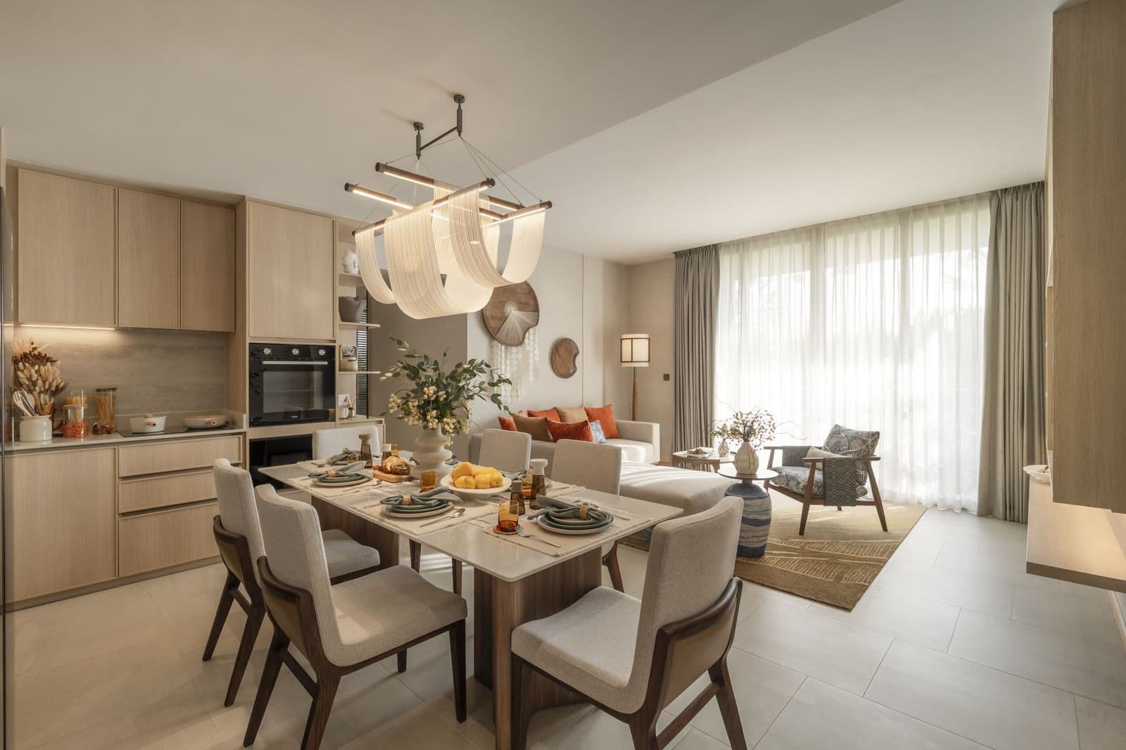 The kitchen and dining area of the finished two-bedroom show unit at PEYLAA Phuket: a table for six, timber cabinets and a built-in oven