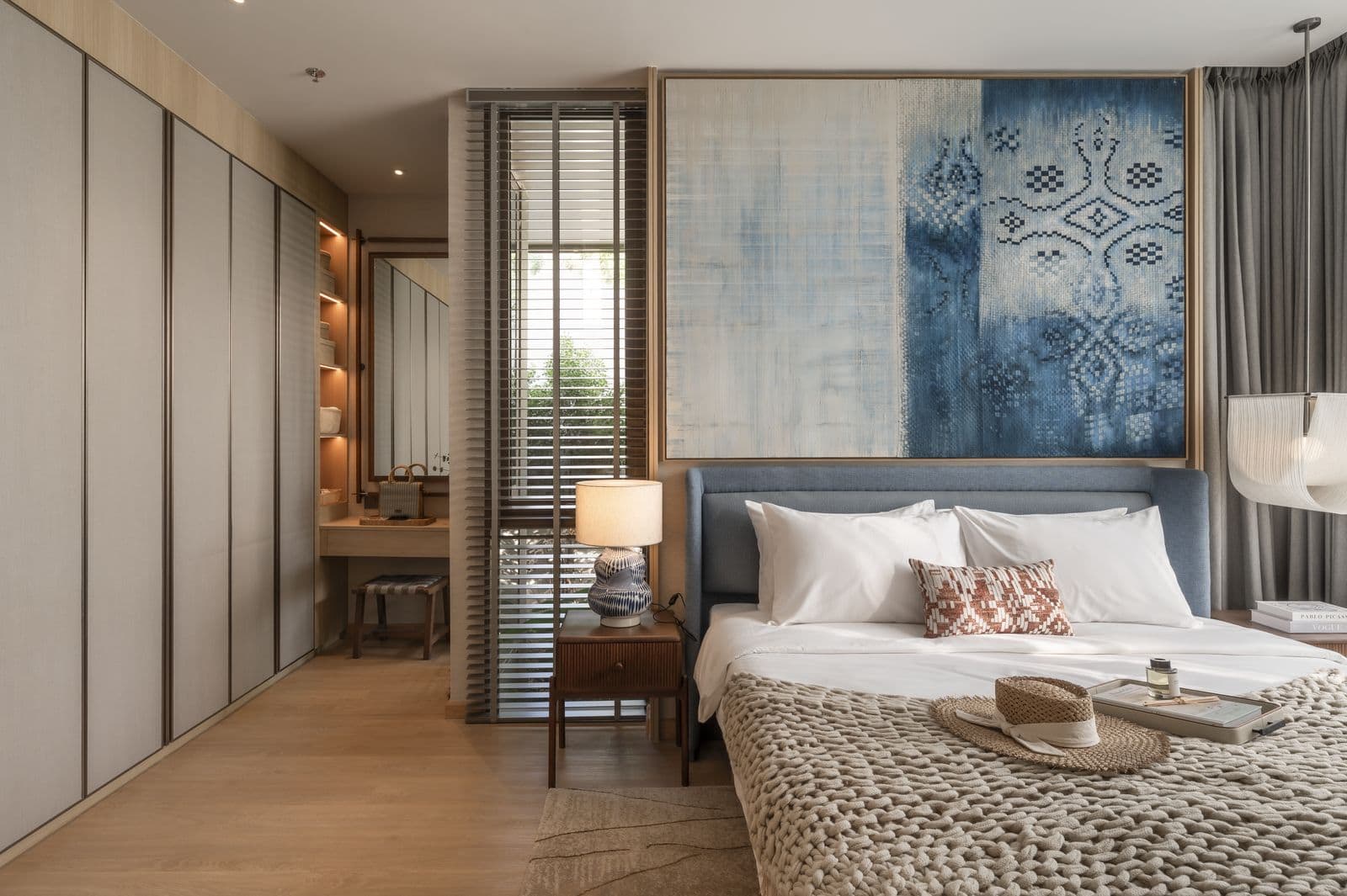 The main bedroom of the finished two-bedroom show unit at PEYLAA Phuket: a king-size bed under a blue woven panel, a dressing table and wardrobes