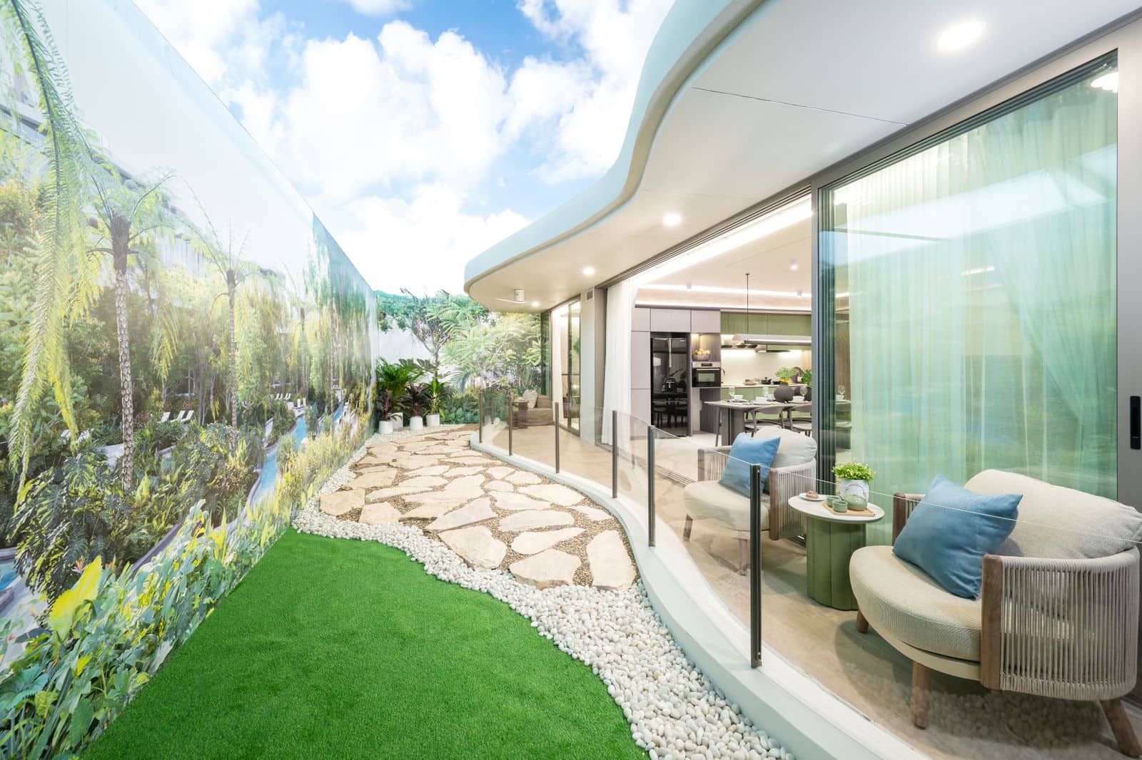 ภาพถ่ายระเบียงสวนของห้องตัวอย่างสองห้องนอนพร้อมเฟอร์นิเจอร์ของ Residences at Garrya Phuket สนามหญ้าและแผ่นทางเดินข้างผนังกระจกของห้องนั่งเล่น