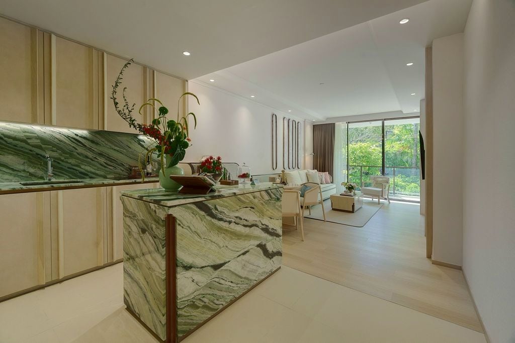 Jade-marble kitchen island and splashback in the furnished one-bedroom show unit of The Residences at InterContinental Phuket Resort, the living room and garden beyond