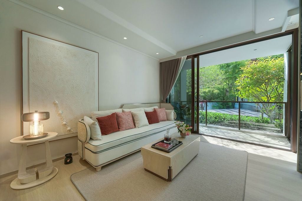 ห้องนั่งเล่นของห้องตัวอย่าง 2 ห้องนอน 100 ตร.ม. ที่ตกแต่งพร้อมอยู่ของ The Residences at InterContinental Phuket Resort ที่สำนักงานขายของ PROUD ประตูกระจกบานเลื่อนเปิดออกสู่ระเบียงและสวน
