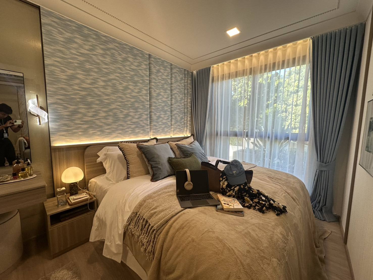 The bedroom of the furnished one-bedroom show unit at Rhea by Sansiri, Surin, Phuket: a double bed with a padded wave-pattern headboard, bedside lamps and a window with curtains