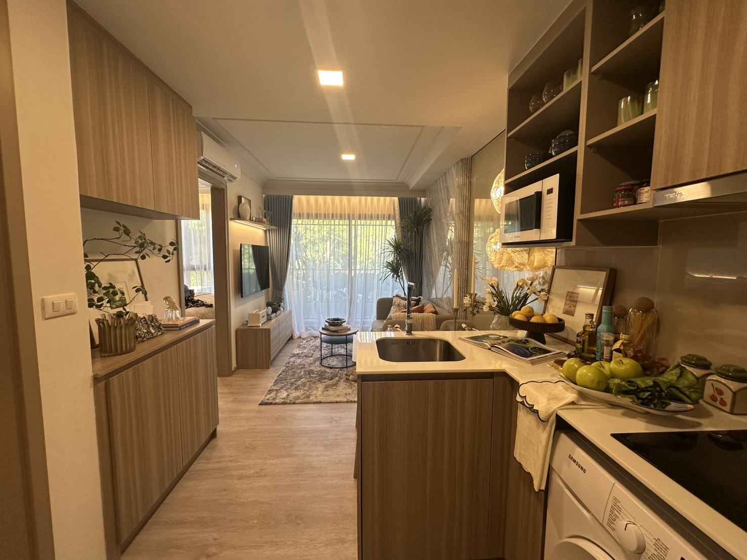 The kitchen of the furnished one-bedroom show unit at Rhea by Sansiri, Surin, Phuket: timber cabinets, a sink and hob, a microwave, a washing machine and a refrigerator