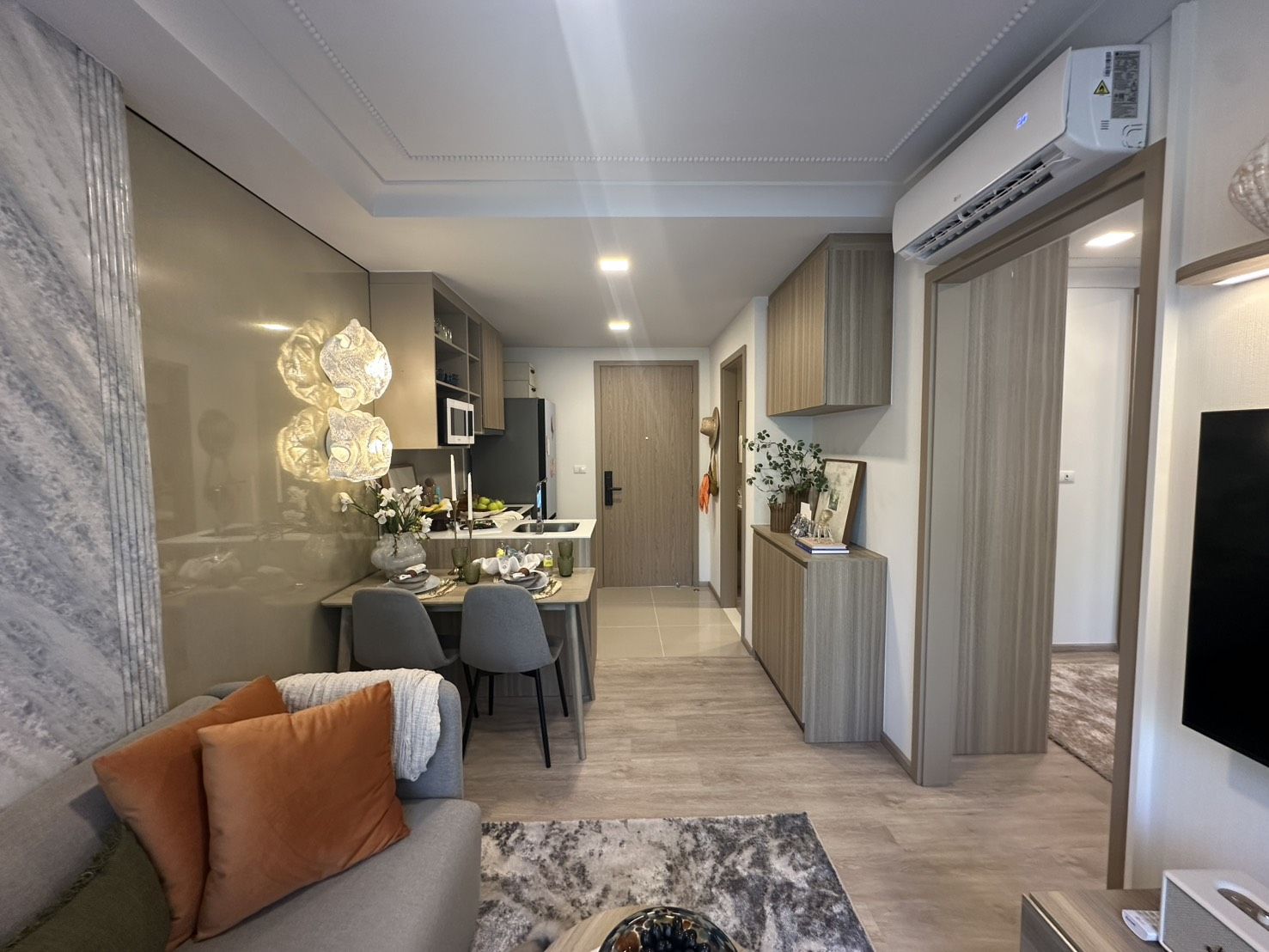 The furnished one-bedroom show unit at Rhea by Sansiri, Surin, Phuket: a dining table for two by the sofa, the kitchen and entrance behind, air conditioning above