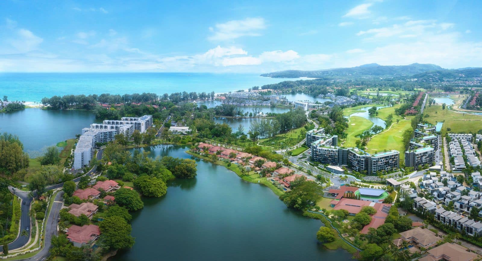 开发商2026年8月拍摄的 Laguna Phuket 园区航拍照片:球场旁是 Skypark Celeste Laguna Phuket 深色的 V 形楼,远处是 Bang Tao 海滩