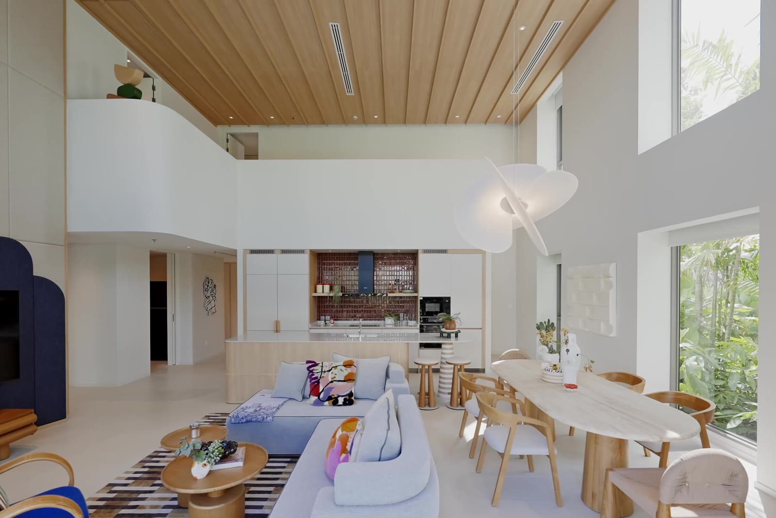 ห้องนั่งเล่นและรับประทานอาหารเพดานสูงสองชั้นของดูเพล็กซ์ตัวอย่างที่ The Standard Residences, Phuket Bang Tao พร้อมฝ้าไม้ ครัวเปิด และหน้าต่างสูงออกสู่สวน