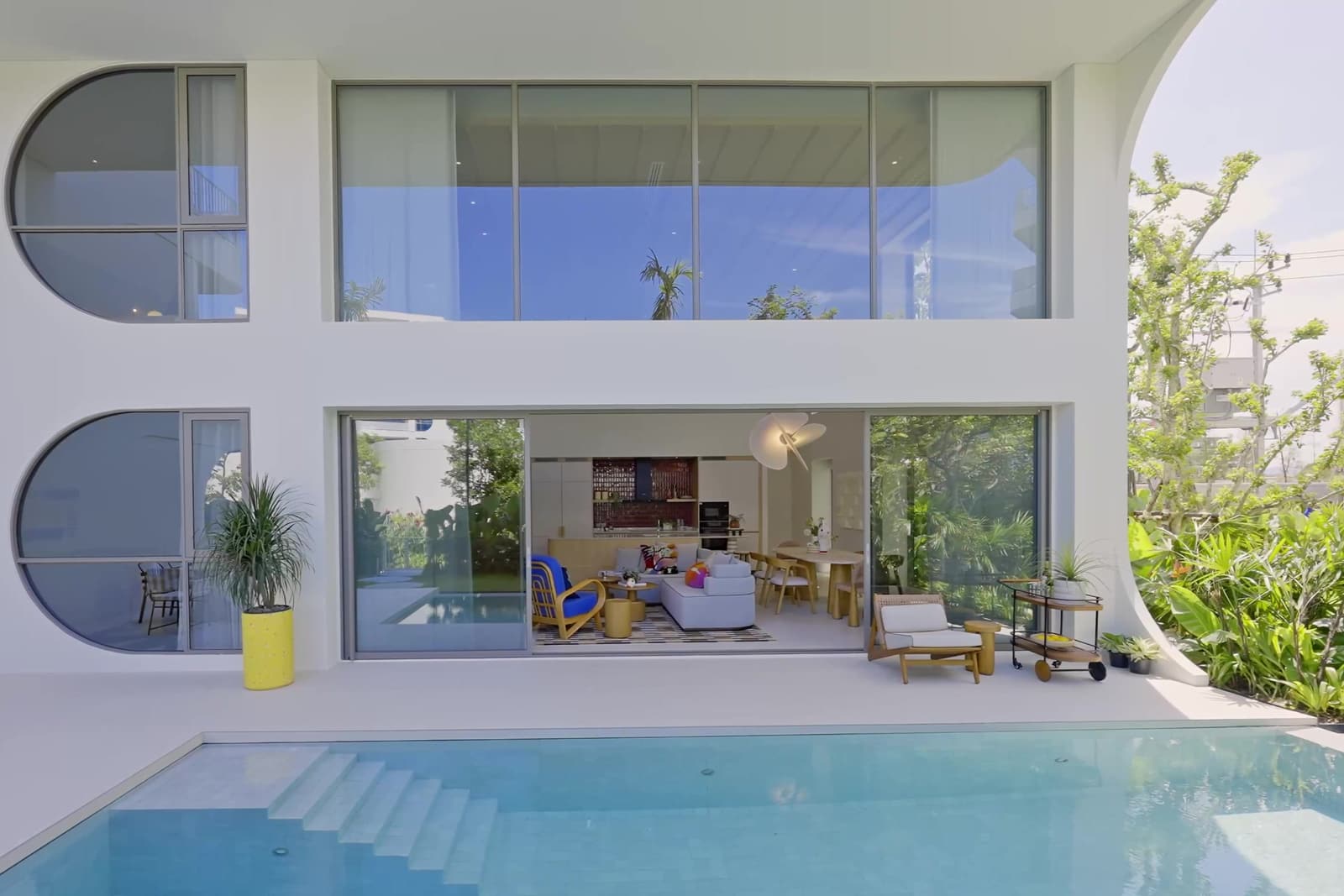 สระส่วนตัวและลานของดูเพล็กซ์ตัวอย่างที่ The Standard Residences, Phuket Bang Tao มองย้อนเข้าไปในห้องนั่งเล่นผ่านประตูกระจก โดยมีหน้าต่างทรงกลมของอาคารอยู่ด้านบน