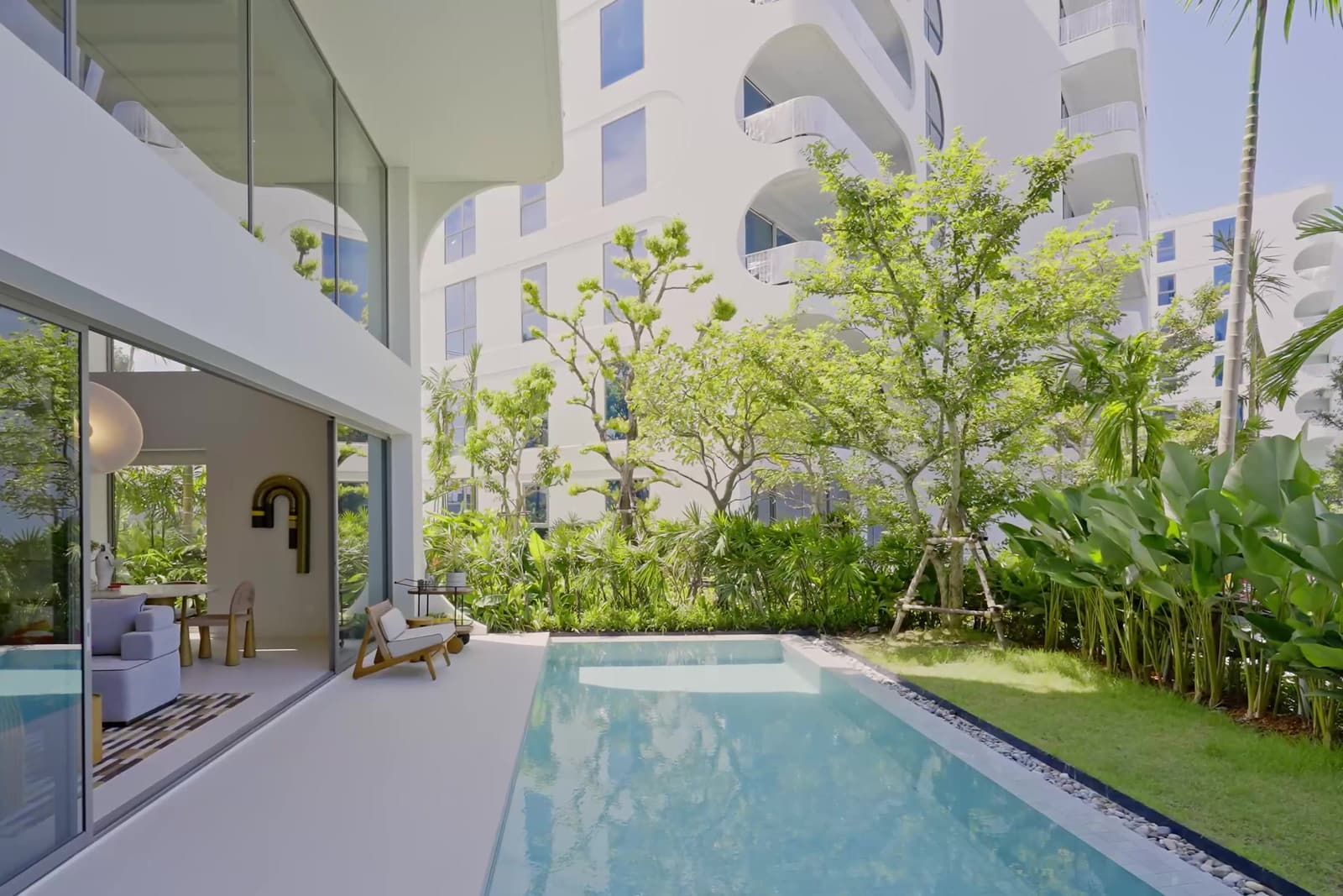 สระส่วนตัวและสนามหญ้าของดูเพล็กซ์ตัวอย่างที่ The Standard Residences, Phuket Bang Tao ท่ามกลางไม้เขตร้อน โดยมีอาคารอยู่ด้านหลัง