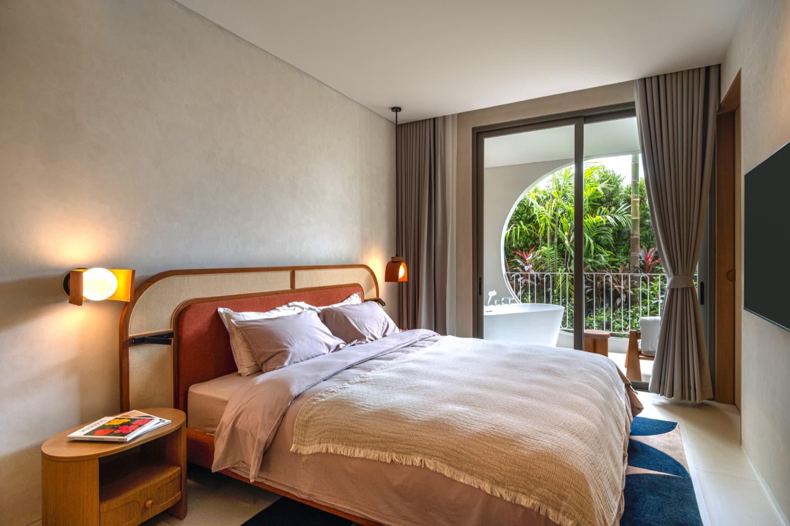 ห้องนอนของห้องตัวอย่าง 1 ห้องนอนที่ The Standard Residences, Phuket Bang Tao พร้อมหน้าต่างทรงกลมมองออกไปยังระเบียงและสวน