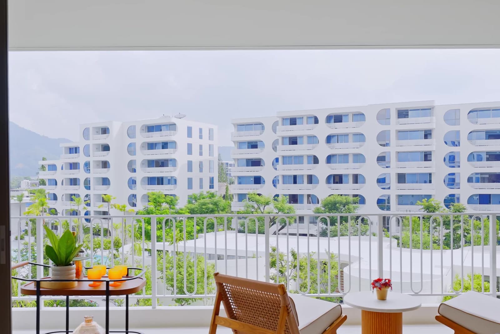 ระเบียงของห้องตัวอย่าง 3 ห้องนอนที่ The Standard Residences, Phuket Bang Tao มองข้ามไปยังอาคารสีขาวที่สร้างเสร็จแล้วของโครงการและแนวเขา