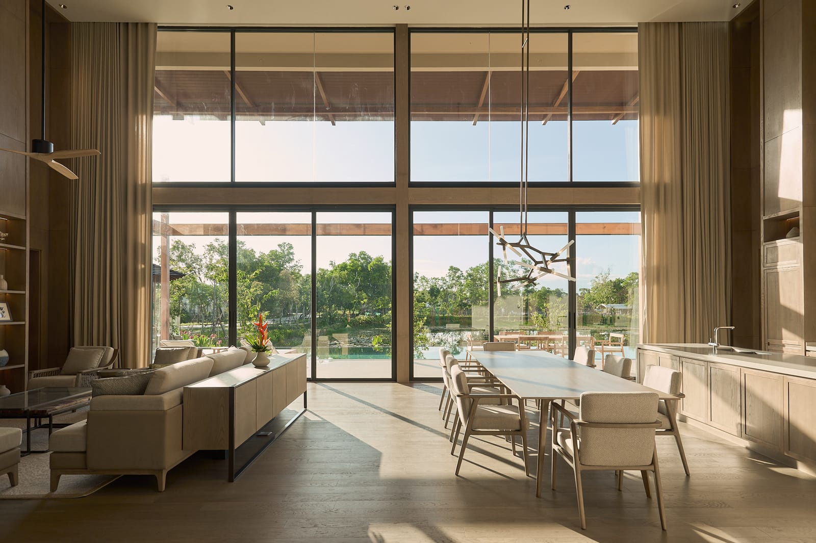 The double-height living and dining room of the Vana 4 show villa at Tri Vananda, Phuket, with full-height glass onto the lake