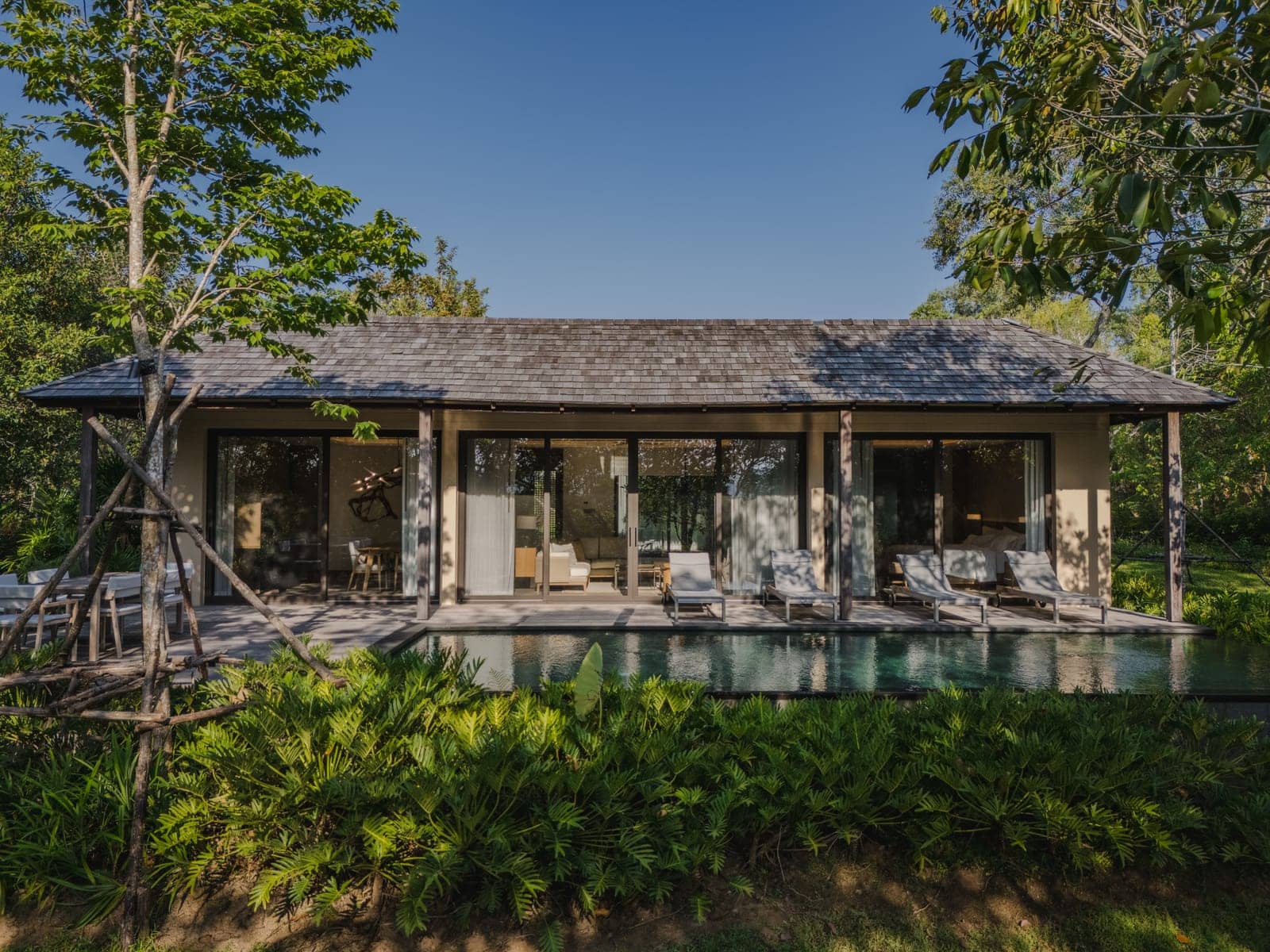 A finished Vana 3 wooden villa at Tri Vananda, Phuket: a low pitched roof, a long pool and the forest behind