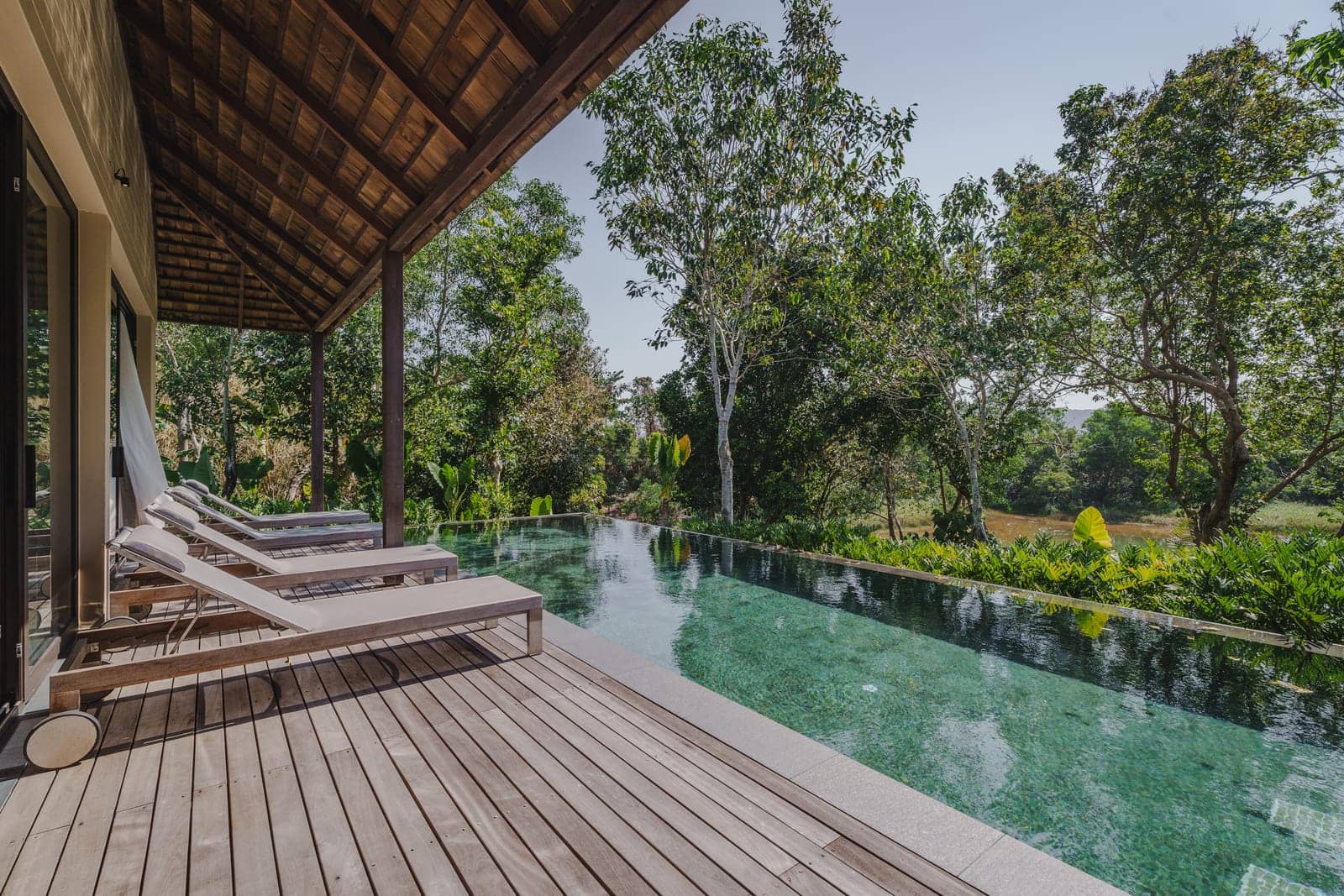 The pool deck of a finished Vana 3 wooden villa at Tri Vananda, Phuket, loungers under the eaves