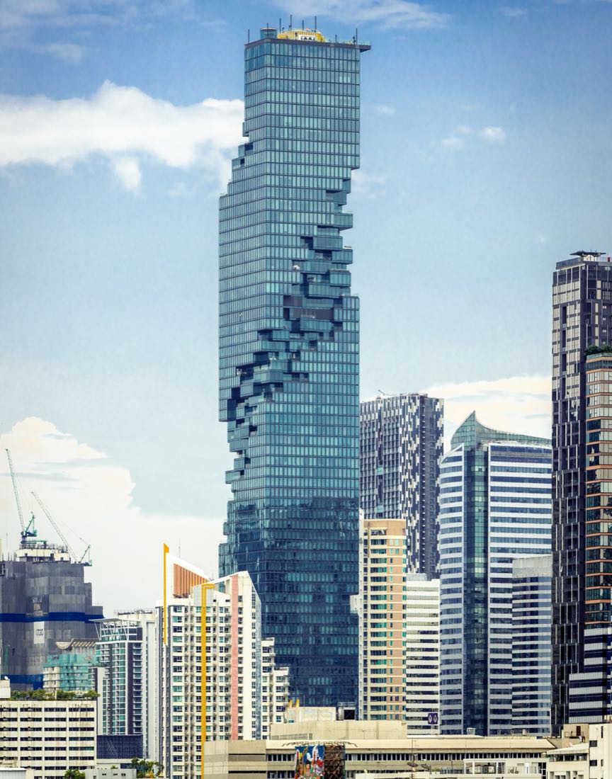 King Power MahaNakhon rising above the Silom and Sathorn skyline in Bangkok, its glass facade broken by a spiral of pixel-like setbacks, with lower towers in front