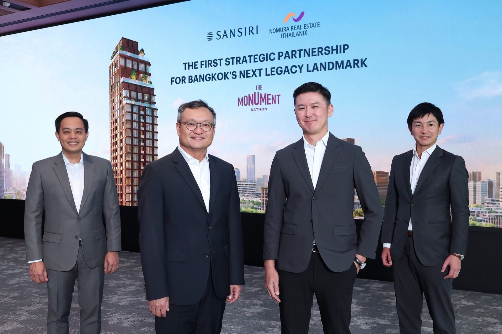 The Monument Sathon 合作公布:四位身穿西裝的男士站在螢幕之前,螢幕上是 Sansiri 與 Nomura Real Estate (Thailand) 的標誌,其下為大樓的電腦效果圖