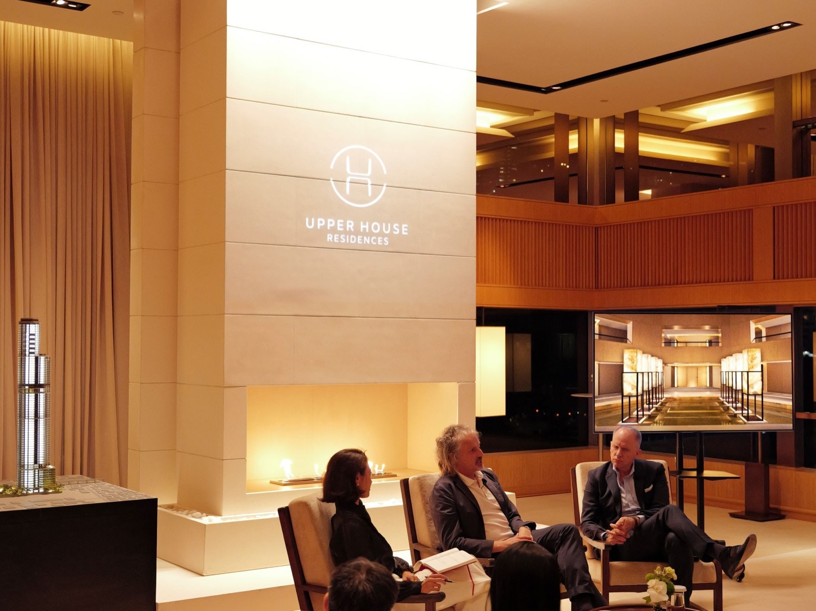 Wireless Road 上的 Upper House Residences 介紹會:壁爐之上亮起 Upper House Residences 的標誌,旁設兩座大樓的建築模型,講者正在對談