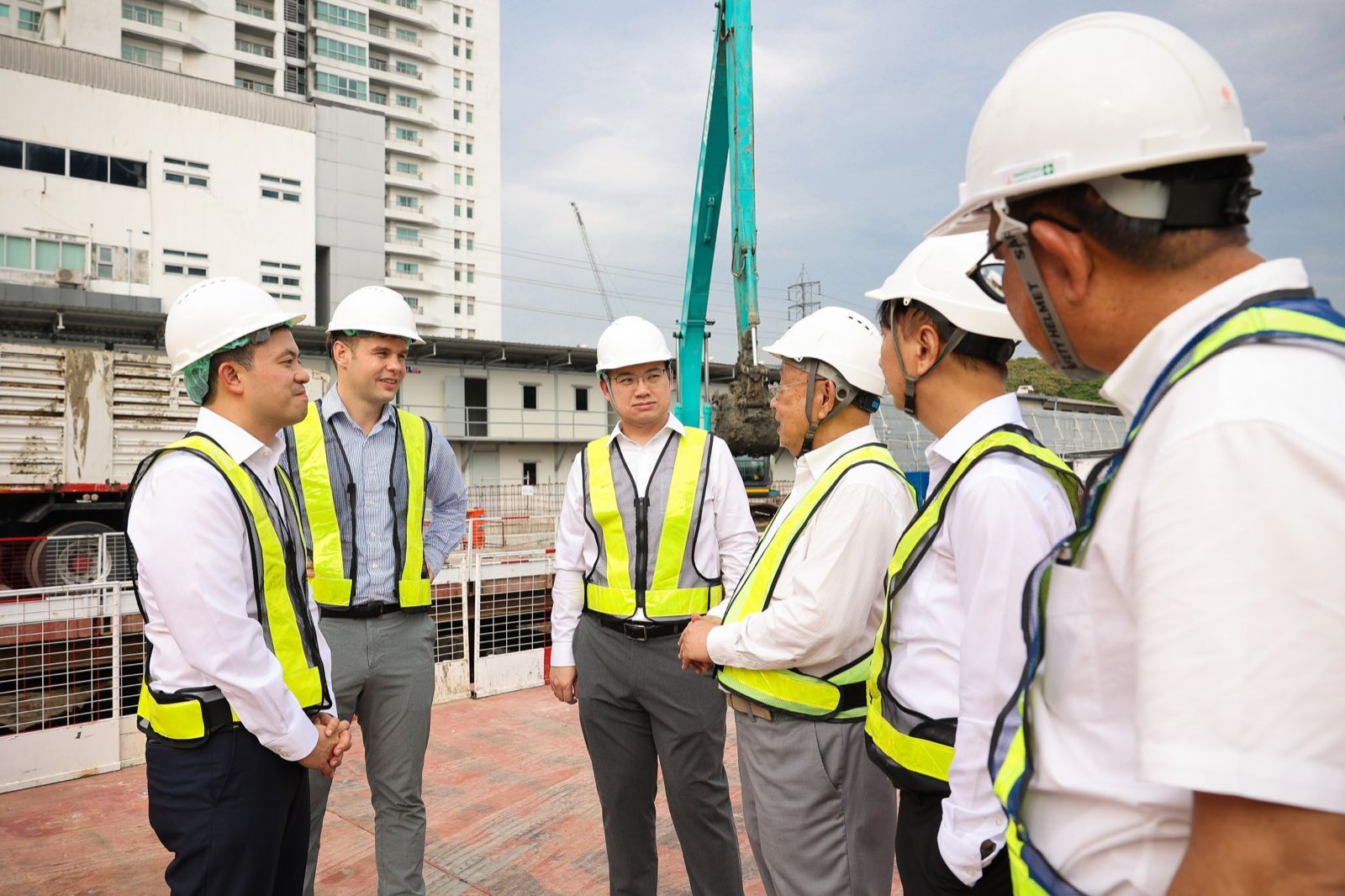 身穿反光背心的管理層在 Wireless Road 上的 Upper House Residences 地盤交談,身後是一台挖土機與曼谷市中心的高樓