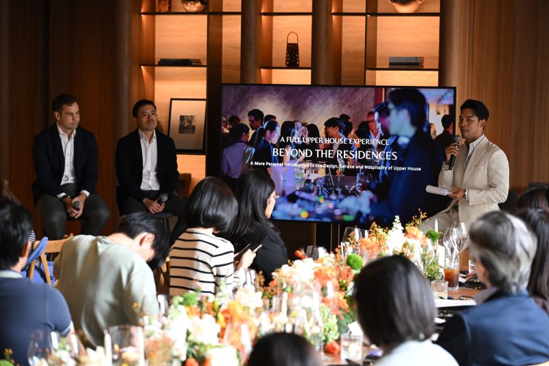 Guests at a flower-lined table watch a speaker present a slide reading A Full Upper House Experience, Beyond the Residences, at the Upper House Residences Bangkok presentation