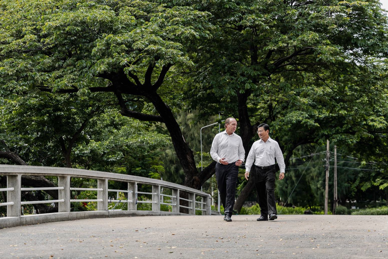 Two executives from City Realty and Swire walk and talk on a bridge through a leafy central Bangkok park