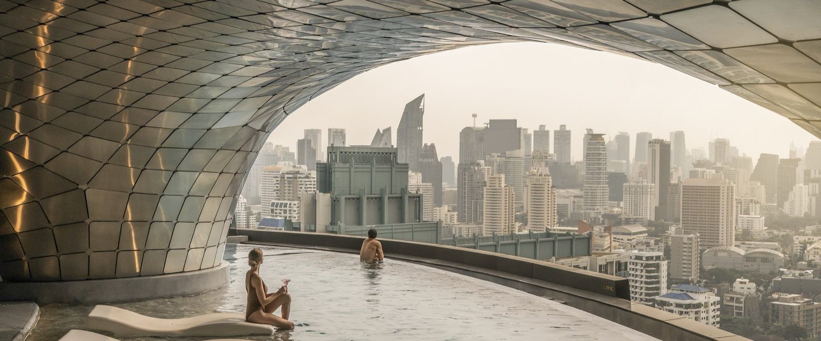 AESTIQ Thonglor: Signature rooftop infinity pool under the gold sculptural canopy, framing a panoramic city view