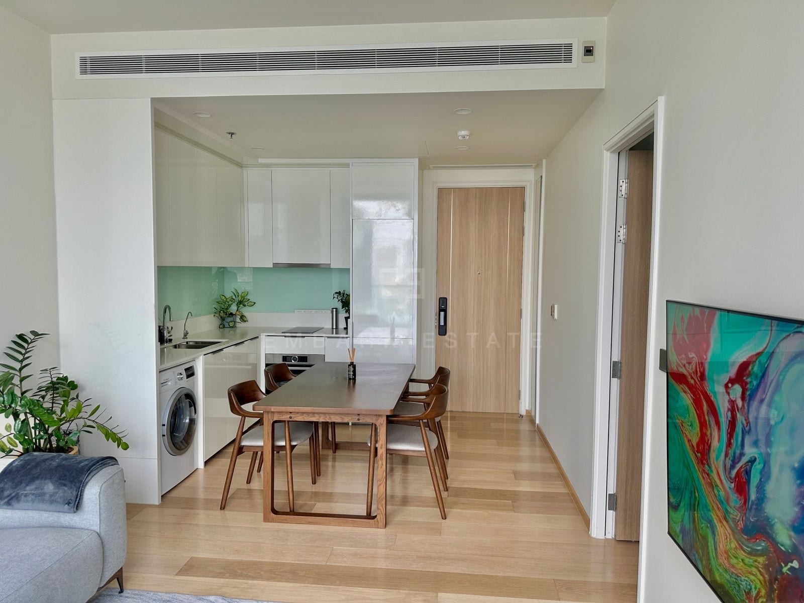 The white open kitchen and dining area of a 1-bedroom residence at ANIL Sathorn 12, Bangkok, with integrated appliances and a timber dining table