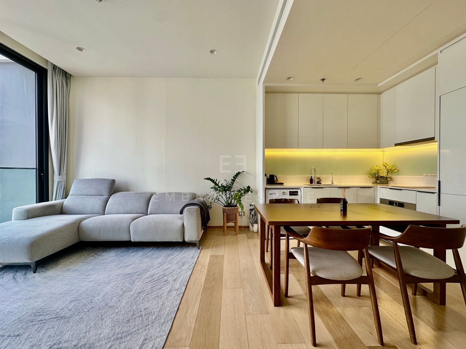 The living and dining area of a 1-bedroom residence at ANIL Sathorn 12, Bangkok, with a sofa, a timber dining table and an open kitchen