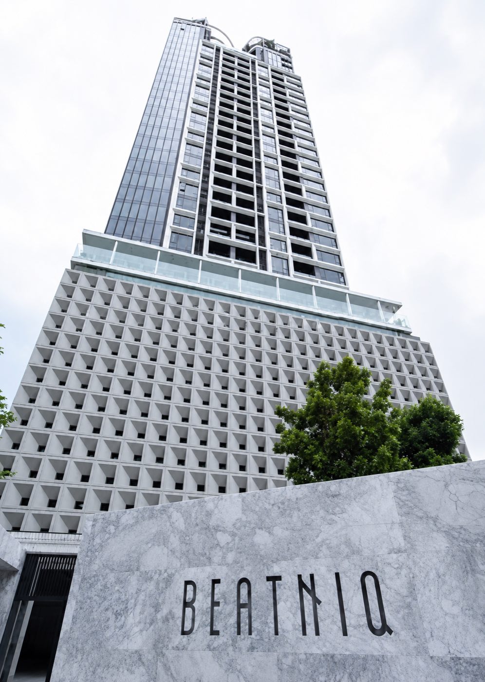 BEATNIQ Sukhumvit 32: the tower rising above the perforated white podium and the BEATNIQ marble signage on Sukhumvit 32 in Bangkok
