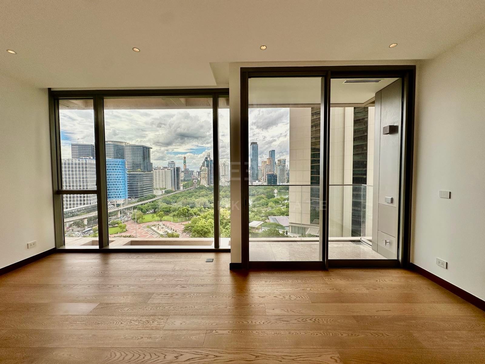 The living room and balcony doors of a two-bedroom residence at Dusit Residences Parkside, Bangkok, opening to a park and skyline view