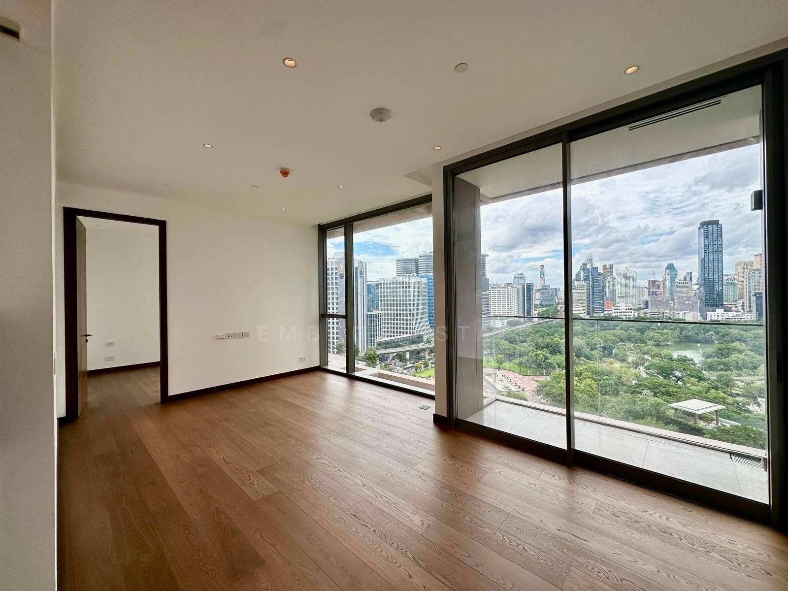 The living room of a two-bedroom residence at Dusit Residences Parkside, Bangkok, unfurnished with oak floors and full-height glass over Lumphini Park and the central Bangkok skyline