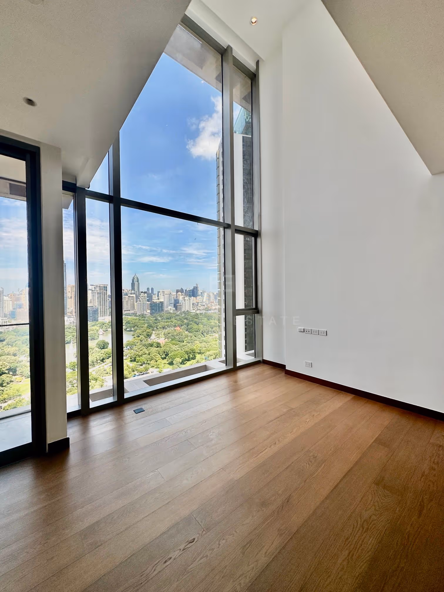 The double-height window of the duplex at Dusit Parkside, Dusit Central Park, framing Lumphini Park, its lake and the Sukhumvit skyline