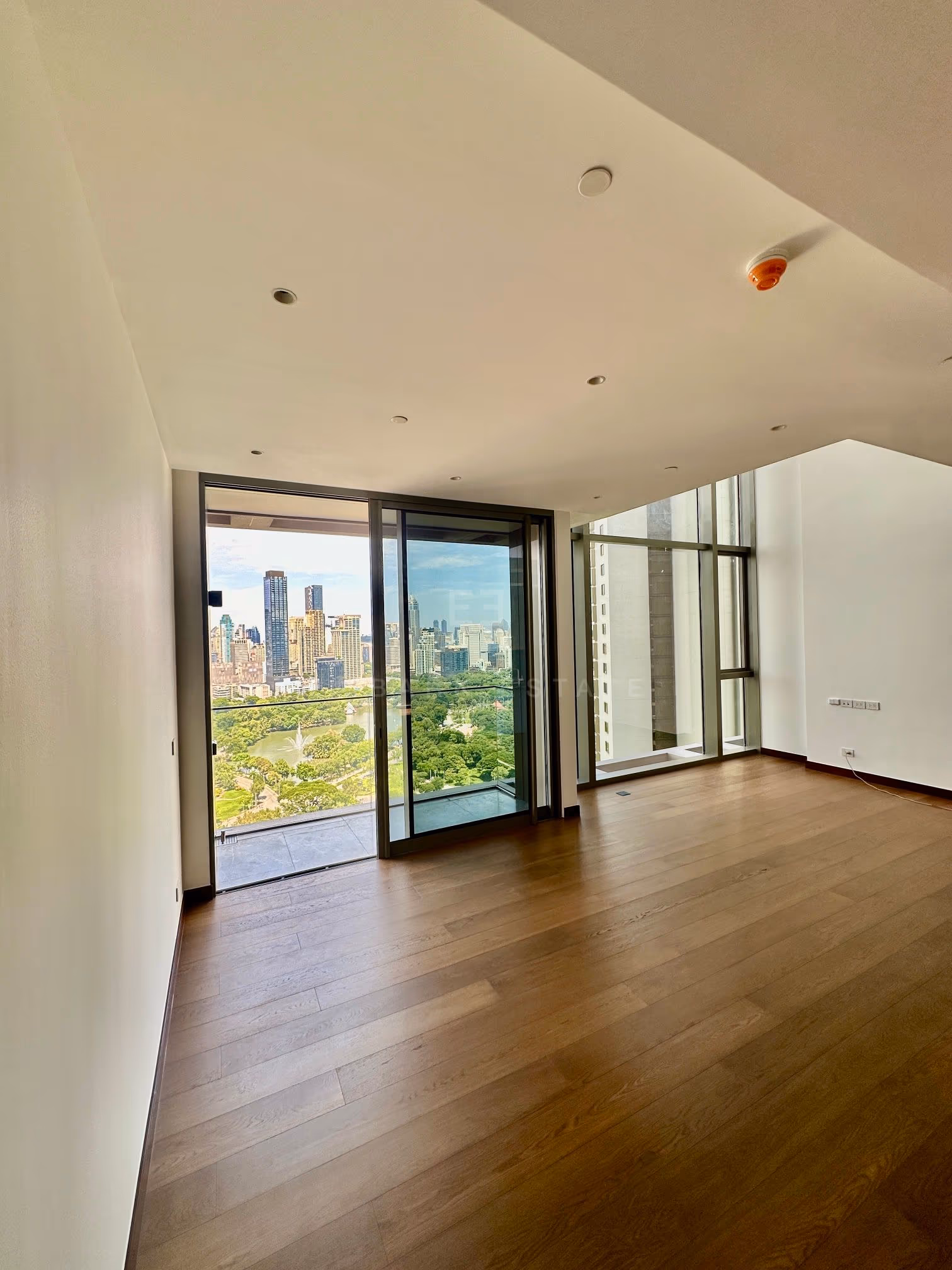 The living room of the duplex at Dusit Parkside, Dusit Central Park, the balcony door open onto Lumphini Park beside the double-height window