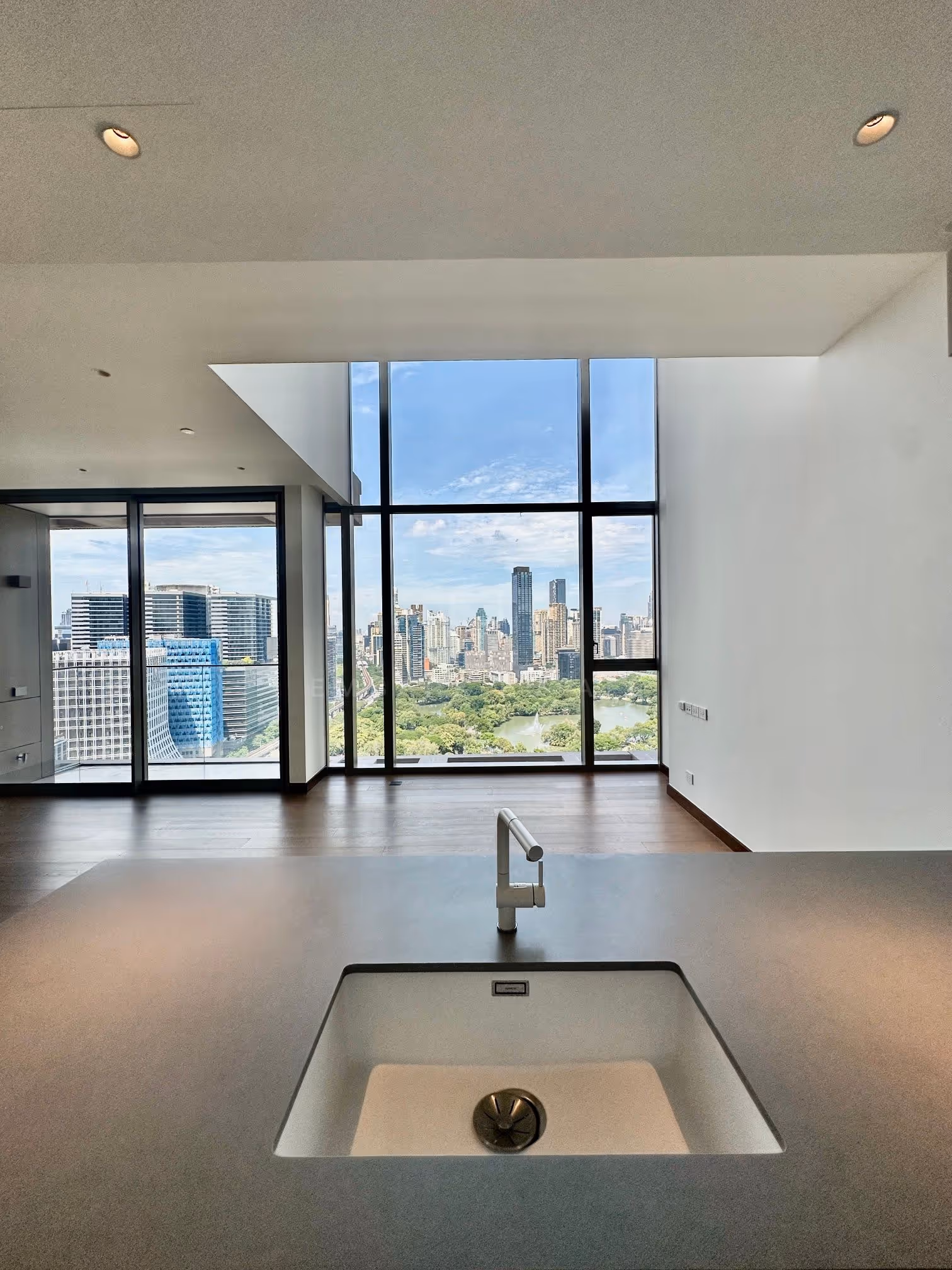 The duplex at Dusit Parkside, Dusit Central Park, seen from the kitchen island across the double-height living room to Lumphini Park and its fountain